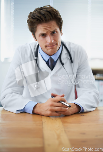 Image of Serious, confused and portrait of doctor in his office for medical consultation at hospital. Doubt, thinking and professional young male healthcare worker with stethoscope by desk at medicare clinic.
