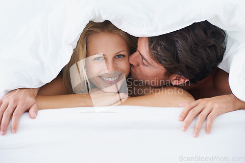 Image of Covers, portrait or happy couple kiss in bed on holiday vacation or romantic honeymoon in marriage. Morning, love or people with smile or joy in home, house or hotel together with duvet, bond or care