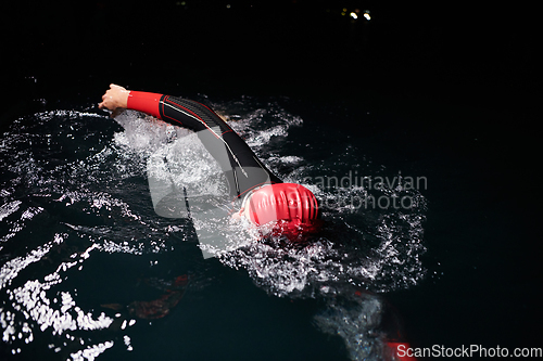 Image of A determined professional triathlete undergoes rigorous night time training in cold waters, showcasing dedication and resilience in preparation for an upcoming triathlon swim competition