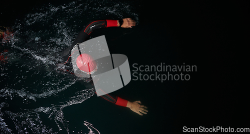 Image of A determined professional triathlete undergoes rigorous night time training in cold waters, showcasing dedication and resilience in preparation for an upcoming triathlon swim competition