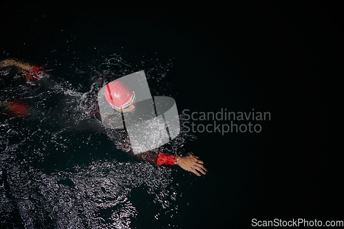 Image of A determined professional triathlete undergoes rigorous night time training in cold waters, showcasing dedication and resilience in preparation for an upcoming triathlon swim competition