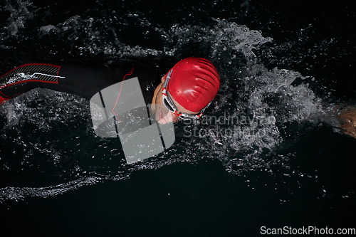 Image of A determined professional triathlete undergoes rigorous night time training in cold waters, showcasing dedication and resilience in preparation for an upcoming triathlon swim competition