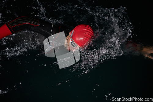 Image of A determined professional triathlete undergoes rigorous night time training in cold waters, showcasing dedication and resilience in preparation for an upcoming triathlon swim competition