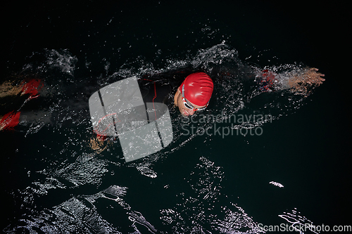 Image of A determined professional triathlete undergoes rigorous night time training in cold waters, showcasing dedication and resilience in preparation for an upcoming triathlon swim competition