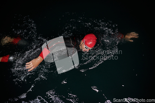 Image of A determined professional triathlete undergoes rigorous night time training in cold waters, showcasing dedication and resilience in preparation for an upcoming triathlon swim competition