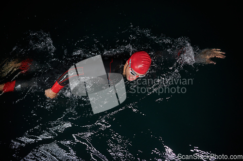 Image of A determined professional triathlete undergoes rigorous night time training in cold waters, showcasing dedication and resilience in preparation for an upcoming triathlon swim competition