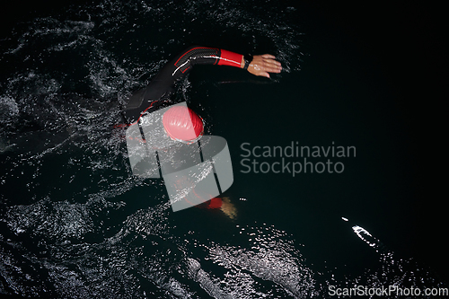 Image of A determined professional triathlete undergoes rigorous night time training in cold waters, showcasing dedication and resilience in preparation for an upcoming triathlon swim competition