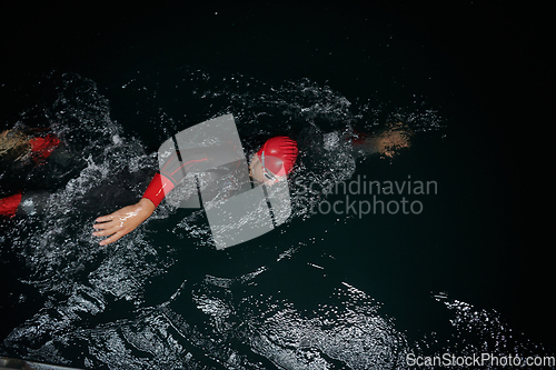 Image of A determined professional triathlete undergoes rigorous night time training in cold waters, showcasing dedication and resilience in preparation for an upcoming triathlon swim competition