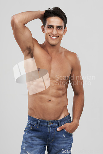 Image of Man, portrait and smile in studio for fashion, confidence and bodybuilder in jeans for style. Male person, shirtless and fitness or muscle progress, face and body care or wellness by gray background