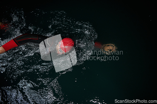 Image of A determined professional triathlete undergoes rigorous night time training in cold waters, showcasing dedication and resilience in preparation for an upcoming triathlon swim competition