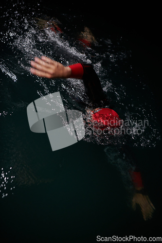 Image of A determined professional triathlete undergoes rigorous night time training in cold waters, showcasing dedication and resilience in preparation for an upcoming triathlon swim competition