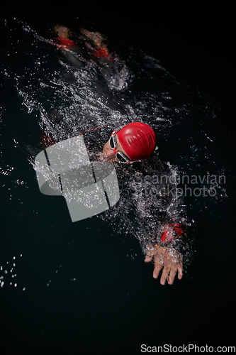 Image of A determined professional triathlete undergoes rigorous night time training in cold waters, showcasing dedication and resilience in preparation for an upcoming triathlon swim competition