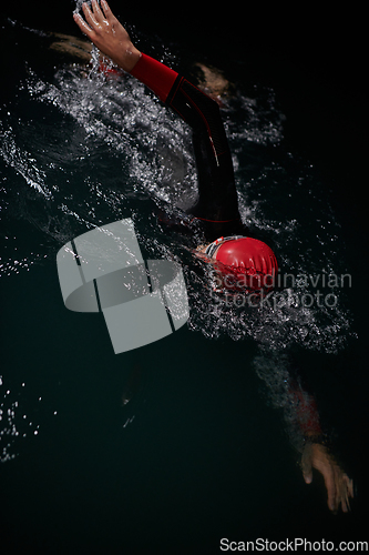 Image of A determined professional triathlete undergoes rigorous night time training in cold waters, showcasing dedication and resilience in preparation for an upcoming triathlon swim competition