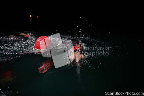 Image of A determined professional triathlete undergoes rigorous night time training in cold waters, showcasing dedication and resilience in preparation for an upcoming triathlon swim competition