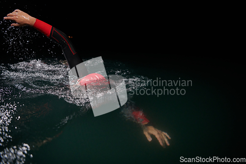 Image of A determined professional triathlete undergoes rigorous night time training in cold waters, showcasing dedication and resilience in preparation for an upcoming triathlon swim competition