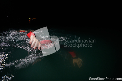 Image of A determined professional triathlete undergoes rigorous night time training in cold waters, showcasing dedication and resilience in preparation for an upcoming triathlon swim competition