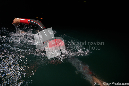 Image of A determined professional triathlete undergoes rigorous night time training in cold waters, showcasing dedication and resilience in preparation for an upcoming triathlon swim competition