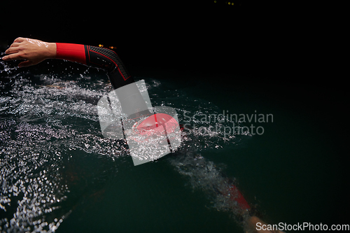 Image of A determined professional triathlete undergoes rigorous night time training in cold waters, showcasing dedication and resilience in preparation for an upcoming triathlon swim competition