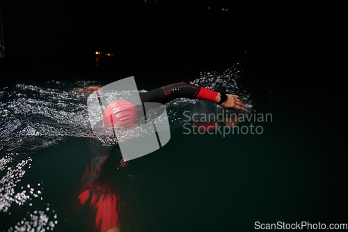 Image of A determined professional triathlete undergoes rigorous night time training in cold waters, showcasing dedication and resilience in preparation for an upcoming triathlon swim competition