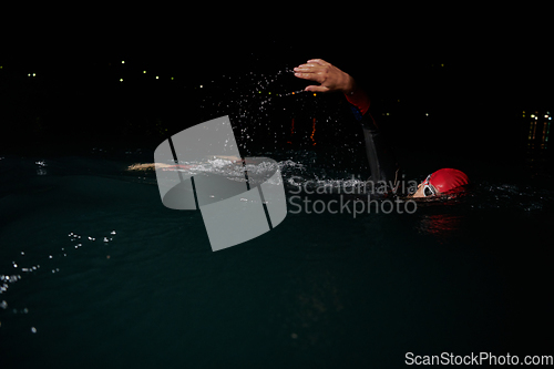 Image of A determined professional triathlete undergoes rigorous night time training in cold waters, showcasing dedication and resilience in preparation for an upcoming triathlon swim competition