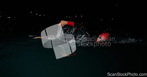 Image of A determined professional triathlete undergoes rigorous night time training in cold waters, showcasing dedication and resilience in preparation for an upcoming triathlon swim competition