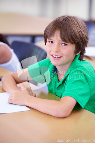 Image of Portrait, happy child or student in classroom for knowledge, education or development for future growth. School, smart boy or clever kid with book, smile or pride for studying or learning at desk