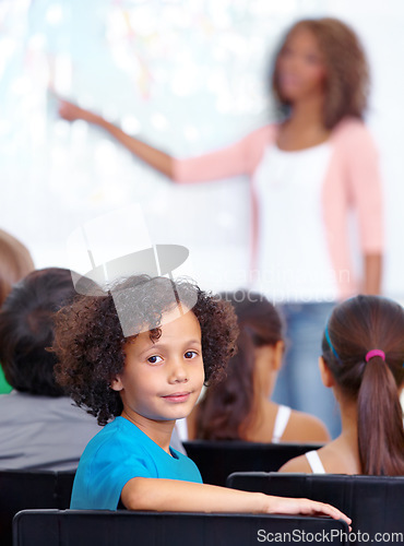 Image of Portrait, boy child or student in classroom for knowledge, education or development for future growth. School, teacher blur or back of a clever kid with book or pride for studying or learning at desk