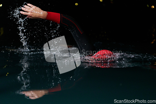 Image of A determined professional triathlete undergoes rigorous night time training in cold waters, showcasing dedication and resilience in preparation for an upcoming triathlon swim competition