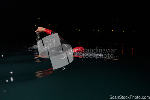 Image of A determined professional triathlete undergoes rigorous night time training in cold waters, showcasing dedication and resilience in preparation for an upcoming triathlon swim competition