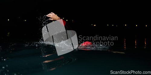 Image of A determined professional triathlete undergoes rigorous night time training in cold waters, showcasing dedication and resilience in preparation for an upcoming triathlon swim competition