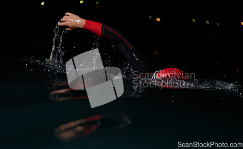 Image of A determined professional triathlete undergoes rigorous night time training in cold waters, showcasing dedication and resilience in preparation for an upcoming triathlon swim competition