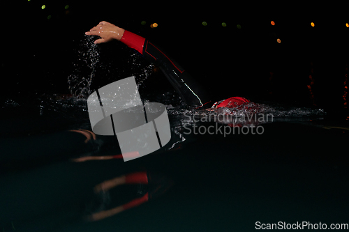 Image of A determined professional triathlete undergoes rigorous night time training in cold waters, showcasing dedication and resilience in preparation for an upcoming triathlon swim competition