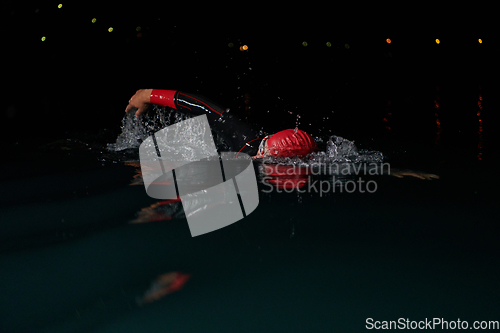 Image of A determined professional triathlete undergoes rigorous night time training in cold waters, showcasing dedication and resilience in preparation for an upcoming triathlon swim competition