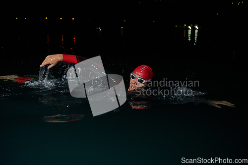 Image of A determined professional triathlete undergoes rigorous night time training in cold waters, showcasing dedication and resilience in preparation for an upcoming triathlon swim competition