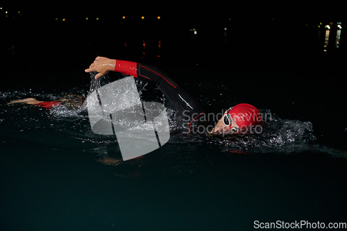 Image of A determined professional triathlete undergoes rigorous night time training in cold waters, showcasing dedication and resilience in preparation for an upcoming triathlon swim competition