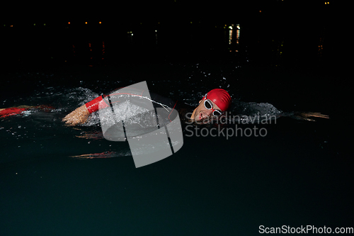 Image of A determined professional triathlete undergoes rigorous night time training in cold waters, showcasing dedication and resilience in preparation for an upcoming triathlon swim competition