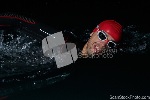 Image of A determined professional triathlete undergoes rigorous night time training in cold waters, showcasing dedication and resilience in preparation for an upcoming triathlon swim competition