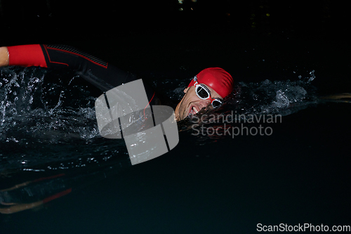 Image of A determined professional triathlete undergoes rigorous night time training in cold waters, showcasing dedication and resilience in preparation for an upcoming triathlon swim competition