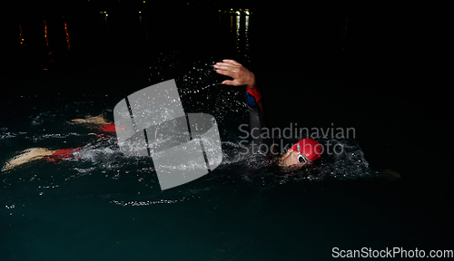 Image of A determined professional triathlete undergoes rigorous night time training in cold waters, showcasing dedication and resilience in preparation for an upcoming triathlon swim competition