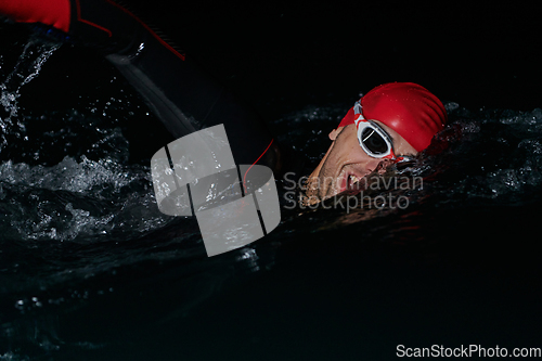 Image of A determined professional triathlete undergoes rigorous night time training in cold waters, showcasing dedication and resilience in preparation for an upcoming triathlon swim competition