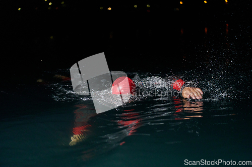 Image of A determined professional triathlete undergoes rigorous night time training in cold waters, showcasing dedication and resilience in preparation for an upcoming triathlon swim competition