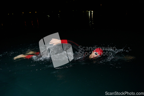 Image of A determined professional triathlete undergoes rigorous night time training in cold waters, showcasing dedication and resilience in preparation for an upcoming triathlon swim competition