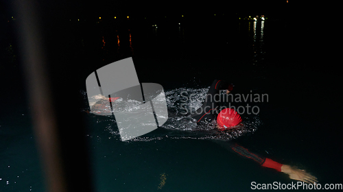 Image of A determined professional triathlete undergoes rigorous night time training in cold waters, showcasing dedication and resilience in preparation for an upcoming triathlon swim competition