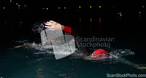 Image of A determined professional triathlete undergoes rigorous night time training in cold waters, showcasing dedication and resilience in preparation for an upcoming triathlon swim competition