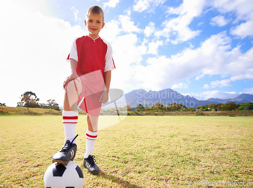 Image of Happy child, soccer ball and sports on green grass for training or practice with clouds and blue sky. Portrait of young football player smile ready for kick off game, match or outdoor field in nature