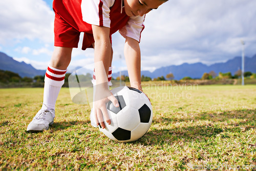 Image of Child, hands and soccer ball for sports on green grass in training or practice with clouds and blue sky. Closeup of young football player ready for kick off game or match on outdoor field in nature