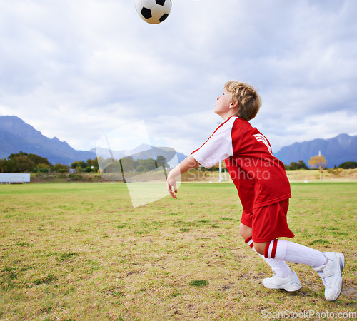 Image of Boy, soccer ball and playing on green grass for sports, training or practice with clouds and blue sky. Young football player, child or kid ready for kick off, game or match on outdoor field in nature