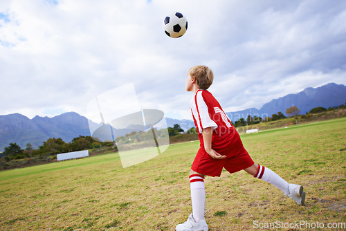 Image of Kid, soccer ball and playing on green grass for sports, training or practice with clouds and blue sky. Young football player or athlete ready for kick off, game or match on outdoor field in nature
