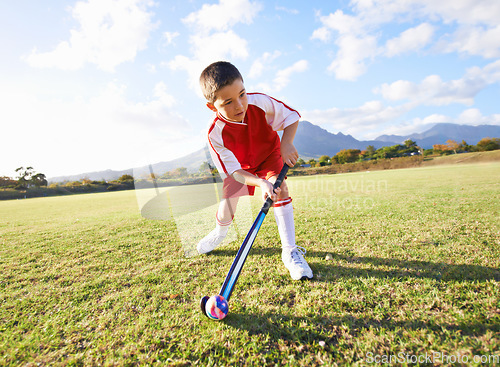 Image of Child, ball and playing hockey on green grass for game, sports or outdoor practice match. Young kid or player enjoying day on field for fitness, activity or training alone in nature with blue sky