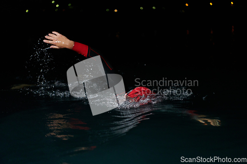 Image of A determined professional triathlete undergoes rigorous night time training in cold waters, showcasing dedication and resilience in preparation for an upcoming triathlon swim competition